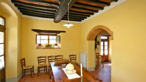 A dining room with a long wooden table, four chairs, a candle, and a window with flowers. - Villa Poggiolino (Subbiano)