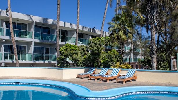 Ein modernes Hotel mit Poolbereich, Liegestühlen und Palmen.