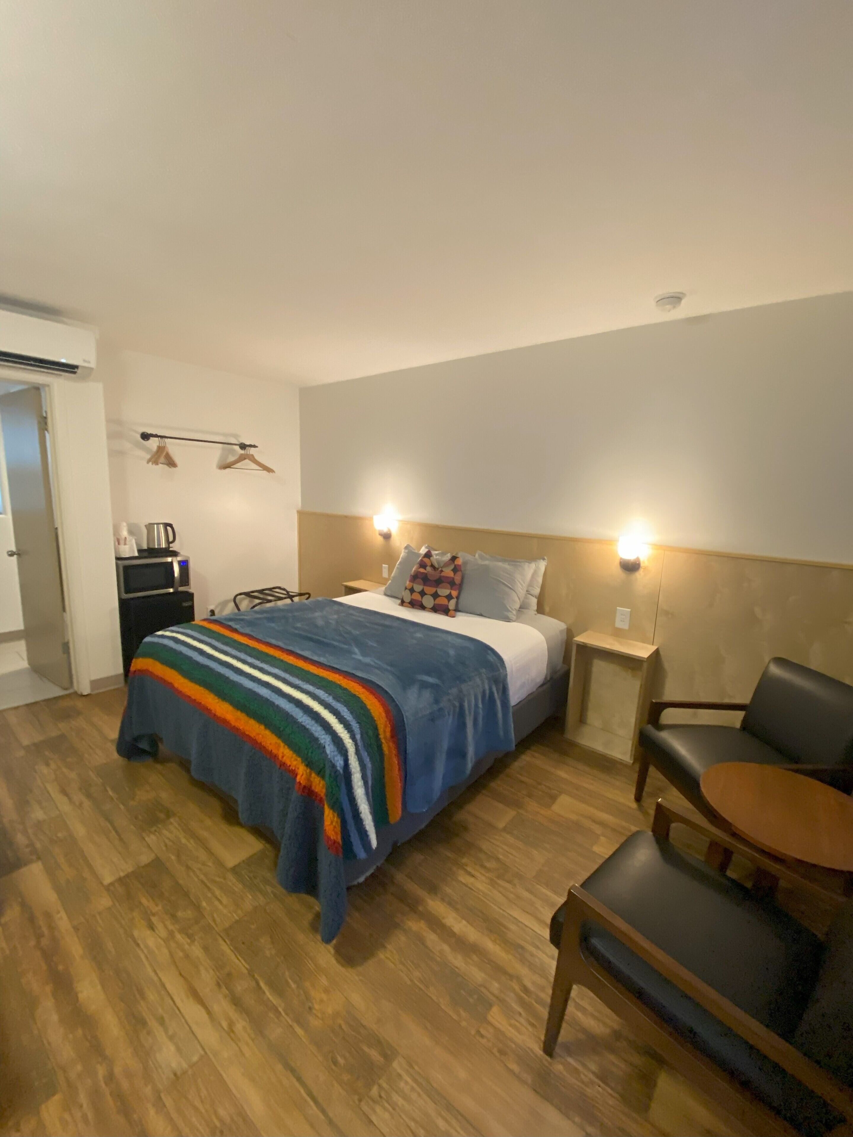 Een hotelkamer met een bed, nachtkastjes, een stoel, een klein tafeltje en een kledingkast.