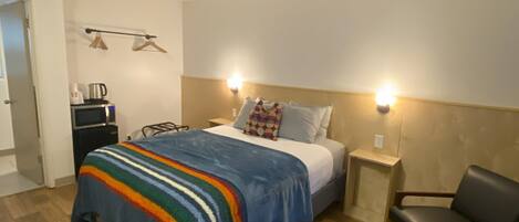 Een hotelkamer met een bed, nachtkastjes, een stoel, een klein tafeltje en een kledingkast.