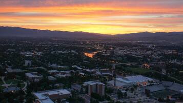 A panoramic view of a city at sunset with buildings and a hilly landscape.