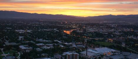 A panoramic view of a city at sunset with buildings and a hilly landscape.