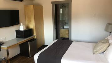 A hotel room with a bed, a desk with a microwave, a TV, and a small fridge.