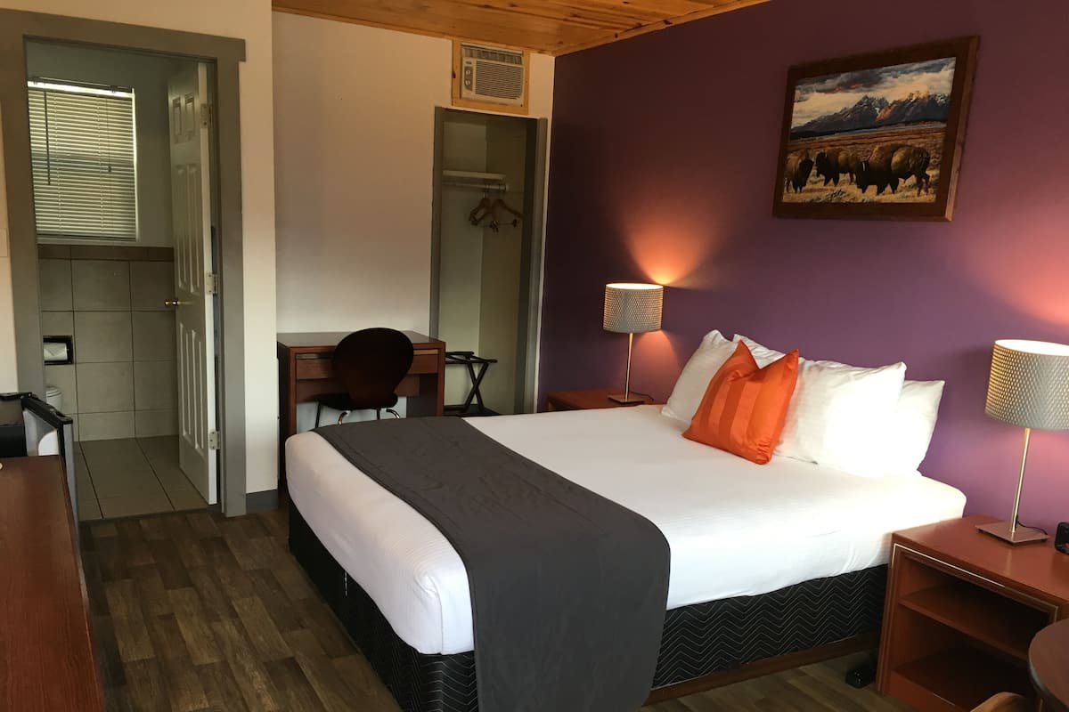Une chambre d’hôtel avec un grand lit, un bureau, une chaise, une armoire et un tableau au mur.