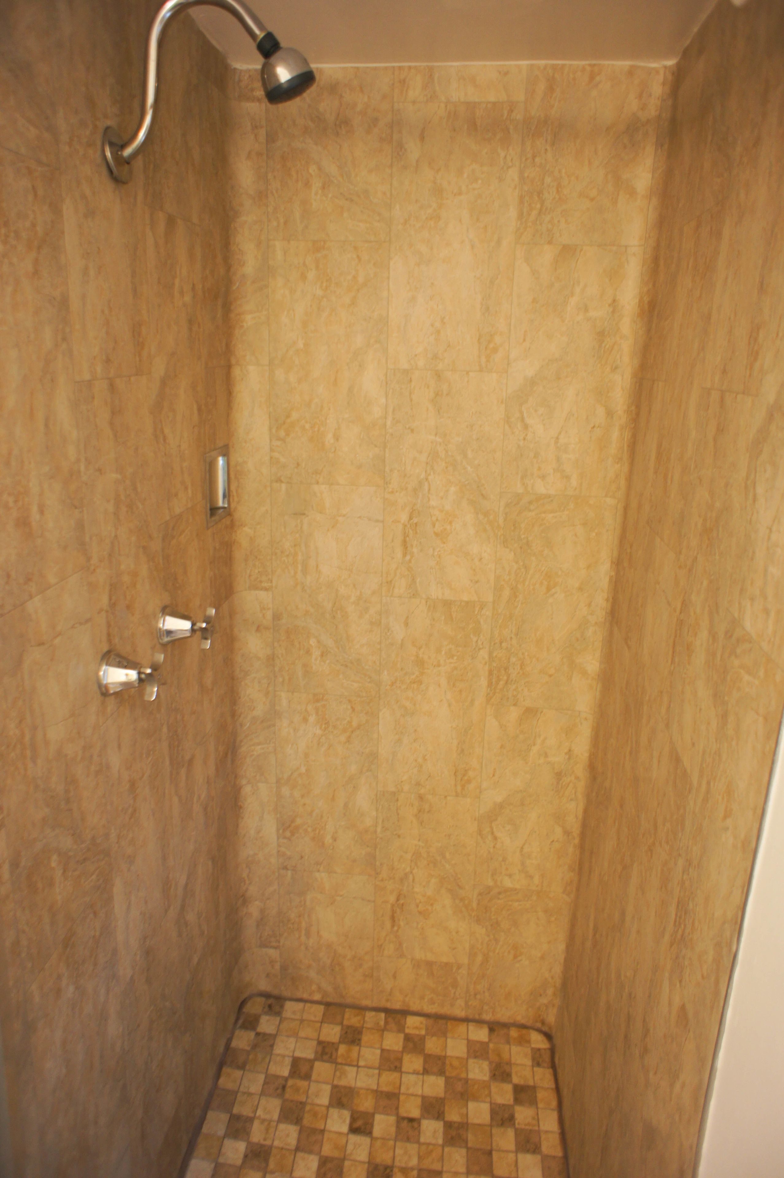 A shower with a checkered floor, a handheld showerhead, and a wall-mounted faucet.