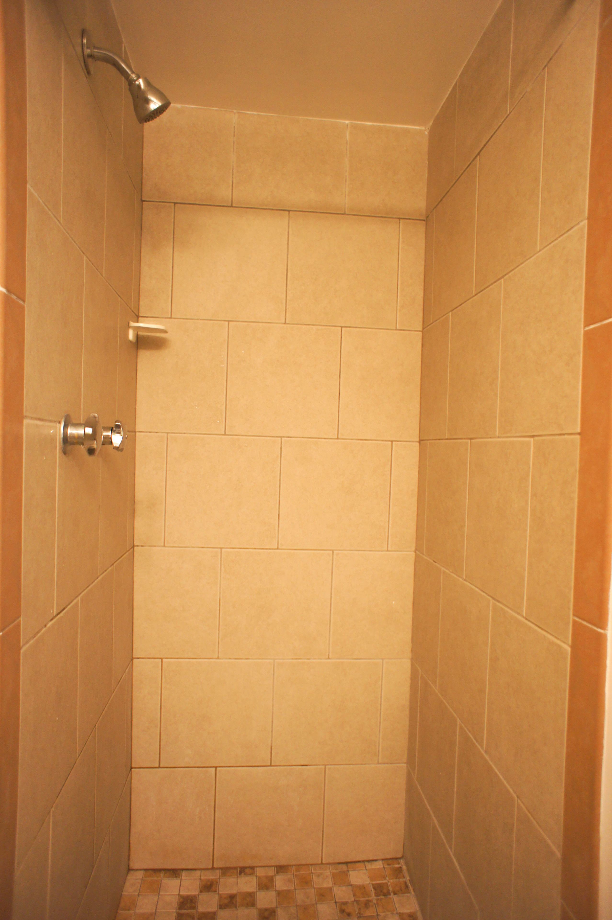 A small, tiled shower room with a showerhead and a door handle.