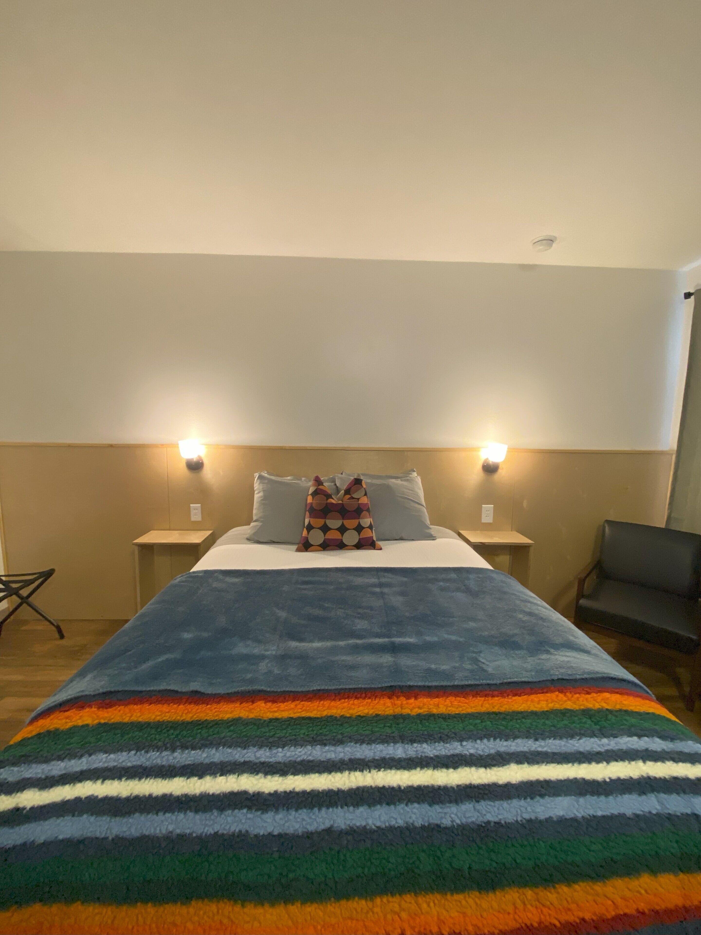 A hotel room with a bed, two bedside lamps, a chair, and a small table.