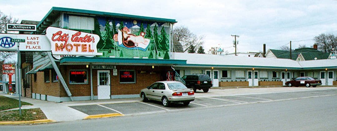 A motel with a large sign reading "City Center Motel," a parking lot, and a building with a green roof.
