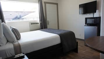 Quarto de hotel com cama, televisão, micro-ondas e janela com cortinas.