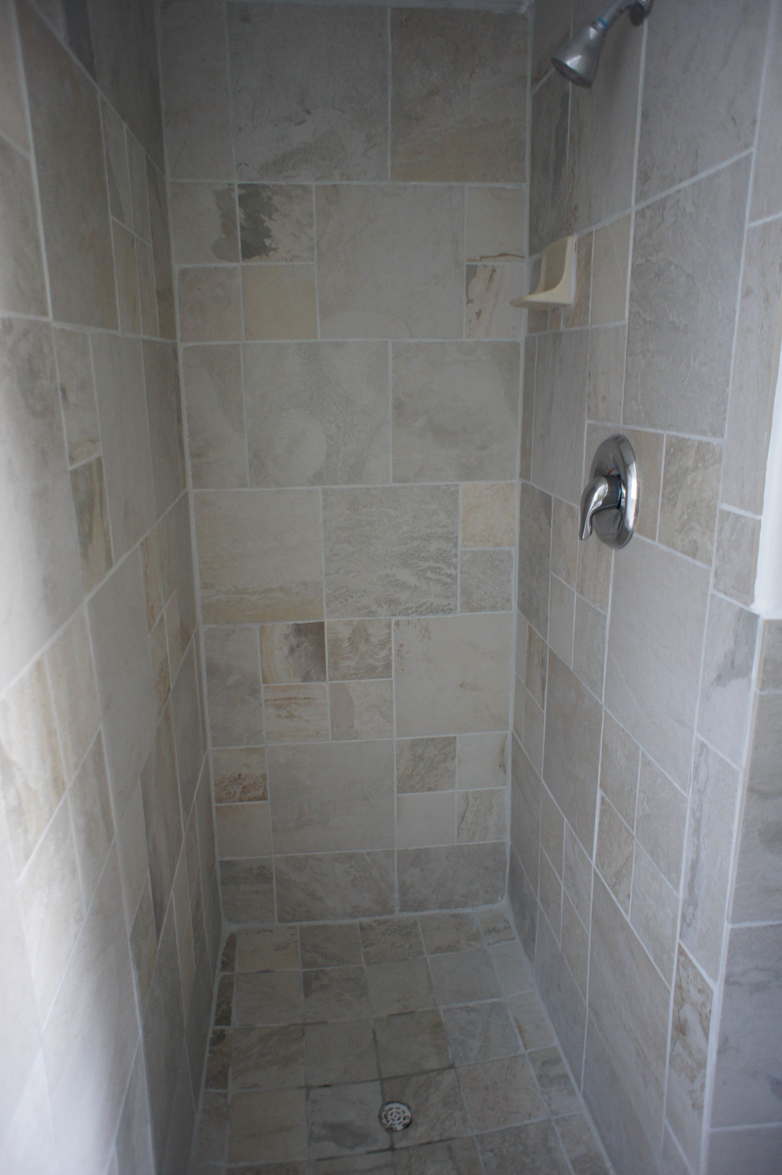 Une petite cabine de douche carrelée, équipée d’un pommeau de douche et d’un drain.