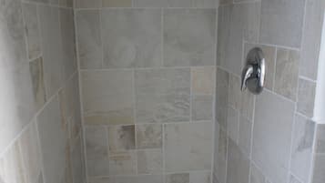 Une petite cabine de douche carrelée, équipée d’un pommeau de douche et d’un drain.