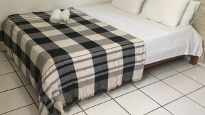 Una cama con una colcha a cuadros, toallas enrolladas, almohadas blancas y un cabecero de madera.