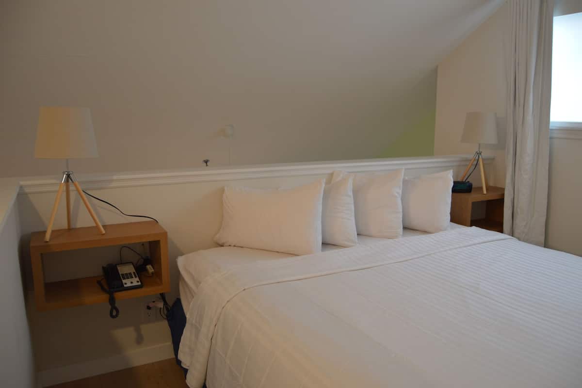 Een slaapkamer met een groot bed, twee nachtkastjes met lampen en een klein plankje met een telefoon.