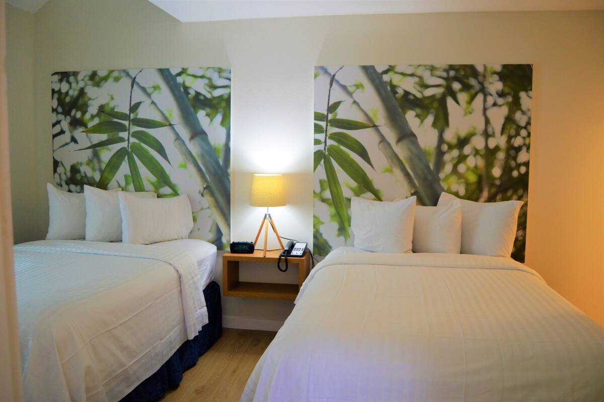 Een hotelkamer met twee bedden, een nachtkastje met een lamp en wanddecoratie waarop bamboe bladeren te zien zijn.