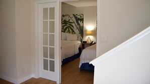 Un dormitorio con una cama, una mesita de noche, una lámpara y una puerta que da a otra habitación.