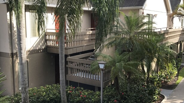 Un edificio residencial con balcón, rodeado de abundante vegetación y un jardín cuidado.