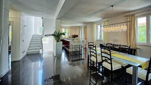 Una cocina amplia con una isla central, un comedor con una mesa larga y sillas, y una escalera que conduce a otro nivel.