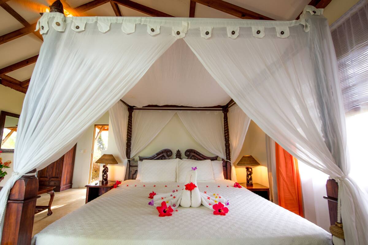 A four-poster canopy bed with a white bedspread and floral arrangements.