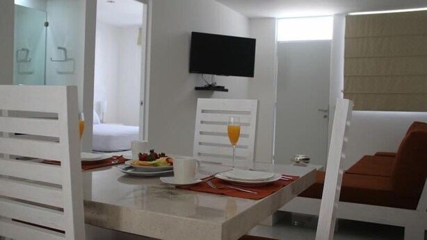 Ein Hotelzimmer mit Essbereich, inklusive Tisch, der für das Frühstück gedeckt ist, einem an der Wand montierten Fernseher und einem Fenster mit Jalousien.