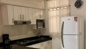 Eine Küche mit weißen Schränken, einer schwarzen Arbeitsplatte, einem weißen Kühlschrank, einer Mikrowelle und einer Uhr an der Wand.