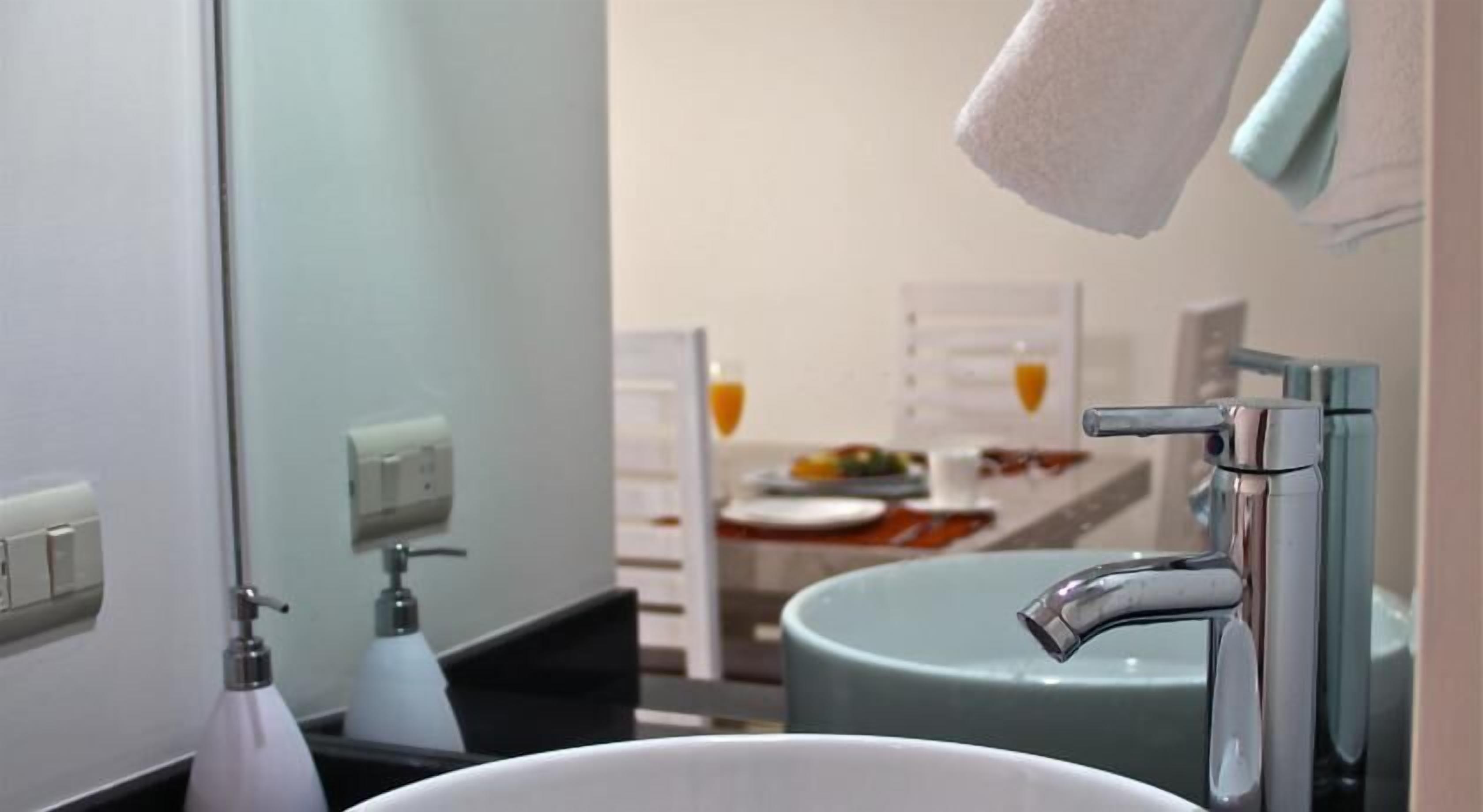 Un baño con un lavamanos blanco, un espejo, una toalla colgada en la pared y una botella de jabón para manos.