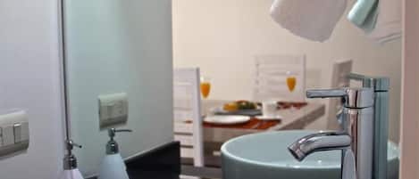 Un baño con un lavamanos blanco, un espejo, una toalla colgada en la pared y una botella de jabón para manos.