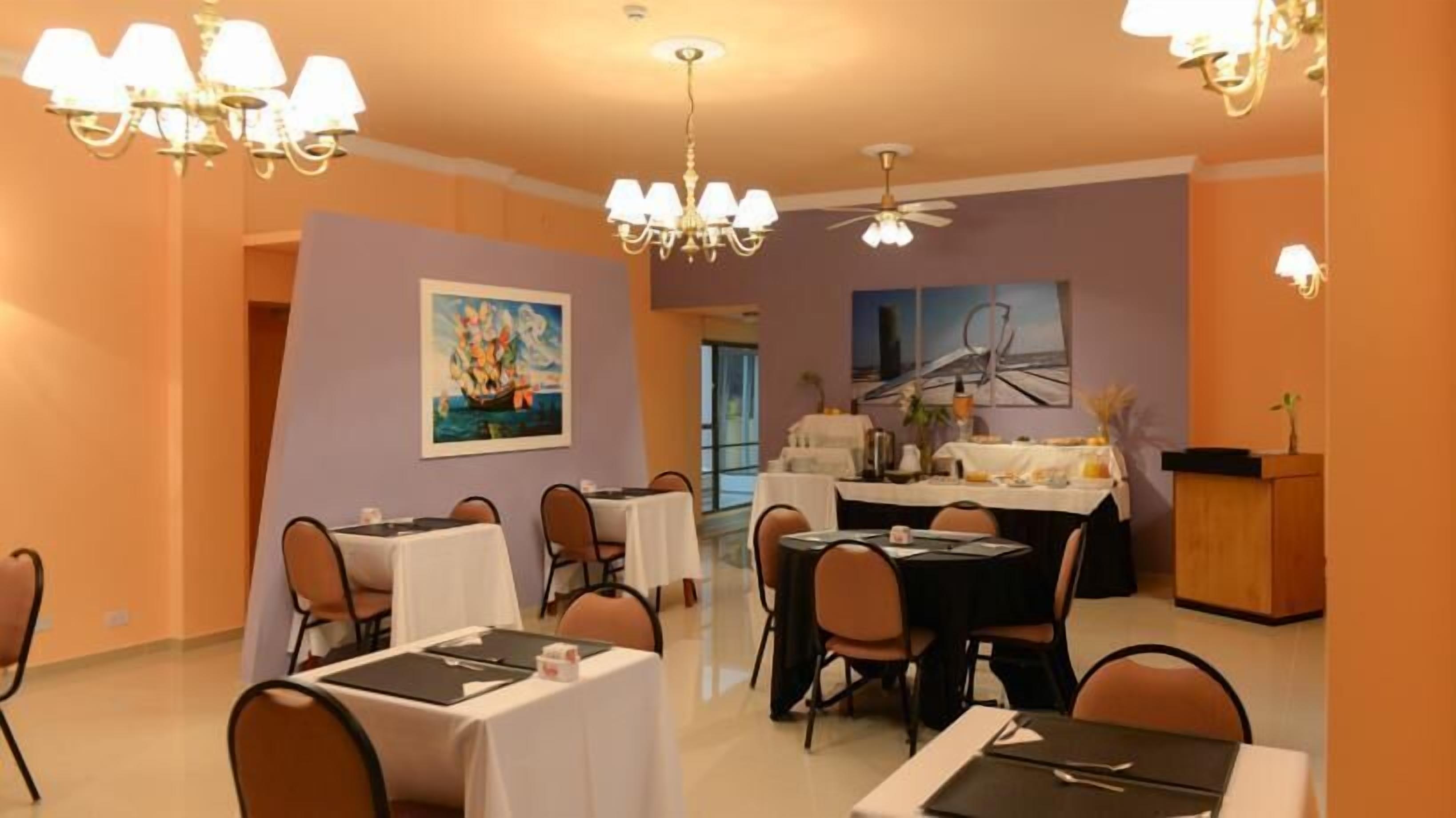 Un comedor con mesas dispuestas para comidas, una araña, ventiladores de techo y obras de arte en las paredes.