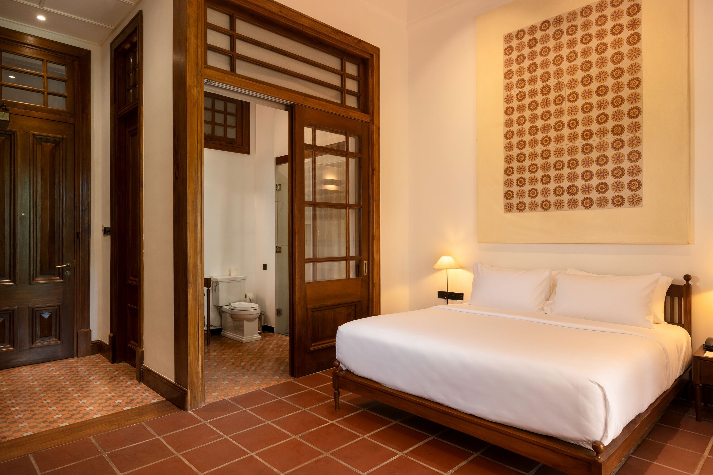 A hotel room with a wooden bed, a large wall-mounted artwork, and a tiled floor.