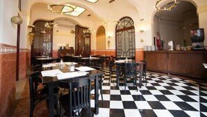 A restaurant with a checkered floor, black and white chairs, and a bar area. - Hotel Peninsular (Barcelona)