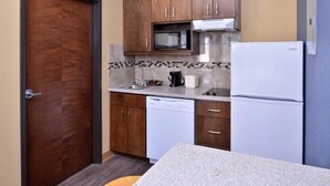 A compact kitchen with wooden cabinets, a microwave, a dishwasher, and a refrigerator. - La Bonita Inn & Suites (Crane)