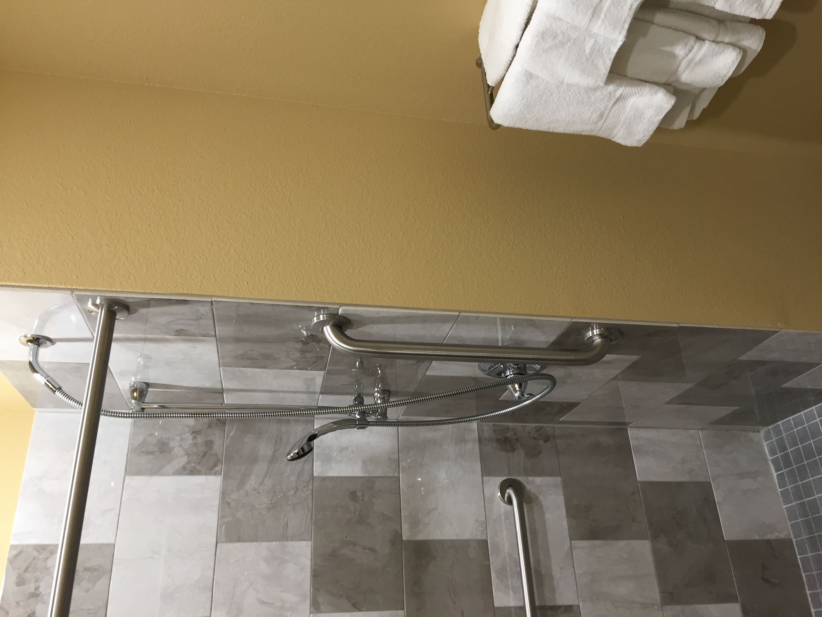 A bathroom with a shower area, grab bars, and a towel rack.