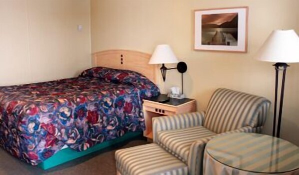 A hotel room with a bed, a desk, a chair, and a lamp.