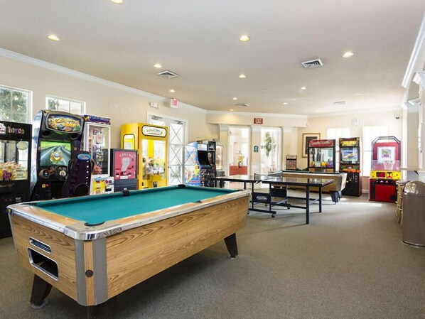 A pool table in a room with arcade games and an exit sign.