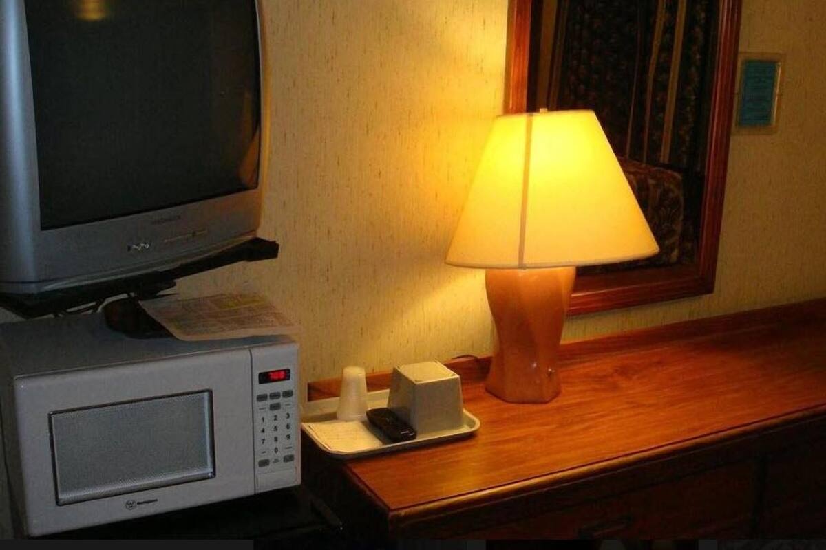 A hotel room with a television, a lamp, a microwave, and a small table with a tray.