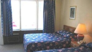 A hotel room with two beds, a window with curtains, a lamp, and a framed picture on the wall. - Shiva's Travelers Lodge (Niagara Falls)