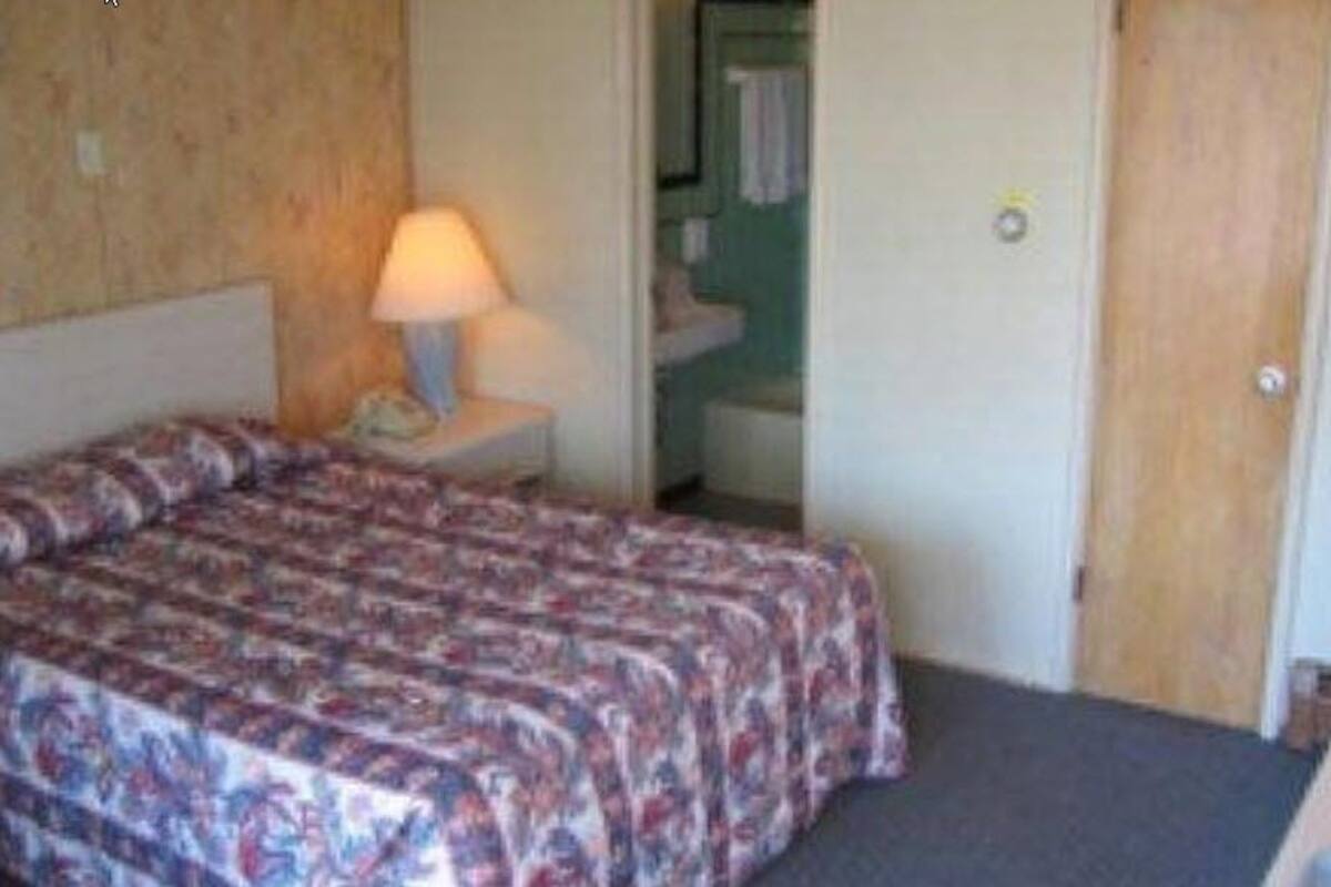 A hotel room with a bed, a nightstand with a lamp, a bathroom visible through an open door, and a television on a stand.