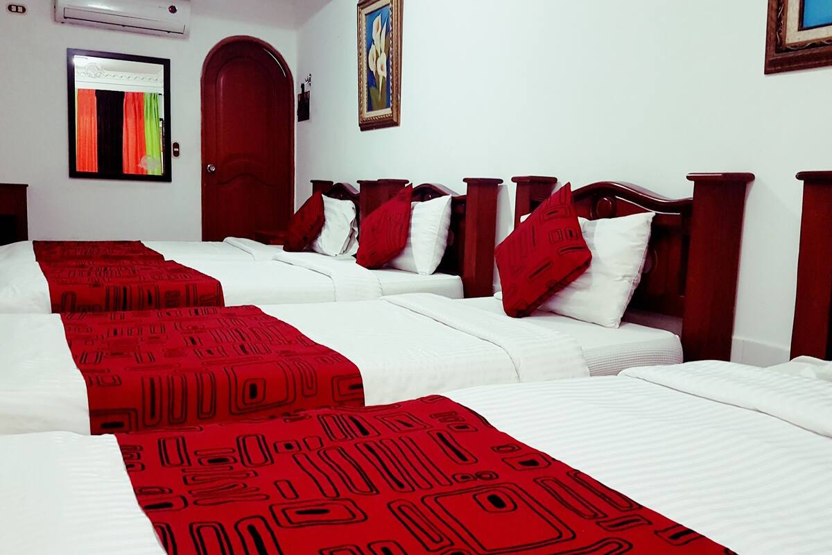 Quarto de hotel com três camas de solteiro, cada uma com colcha estampada em vermelho e branco.