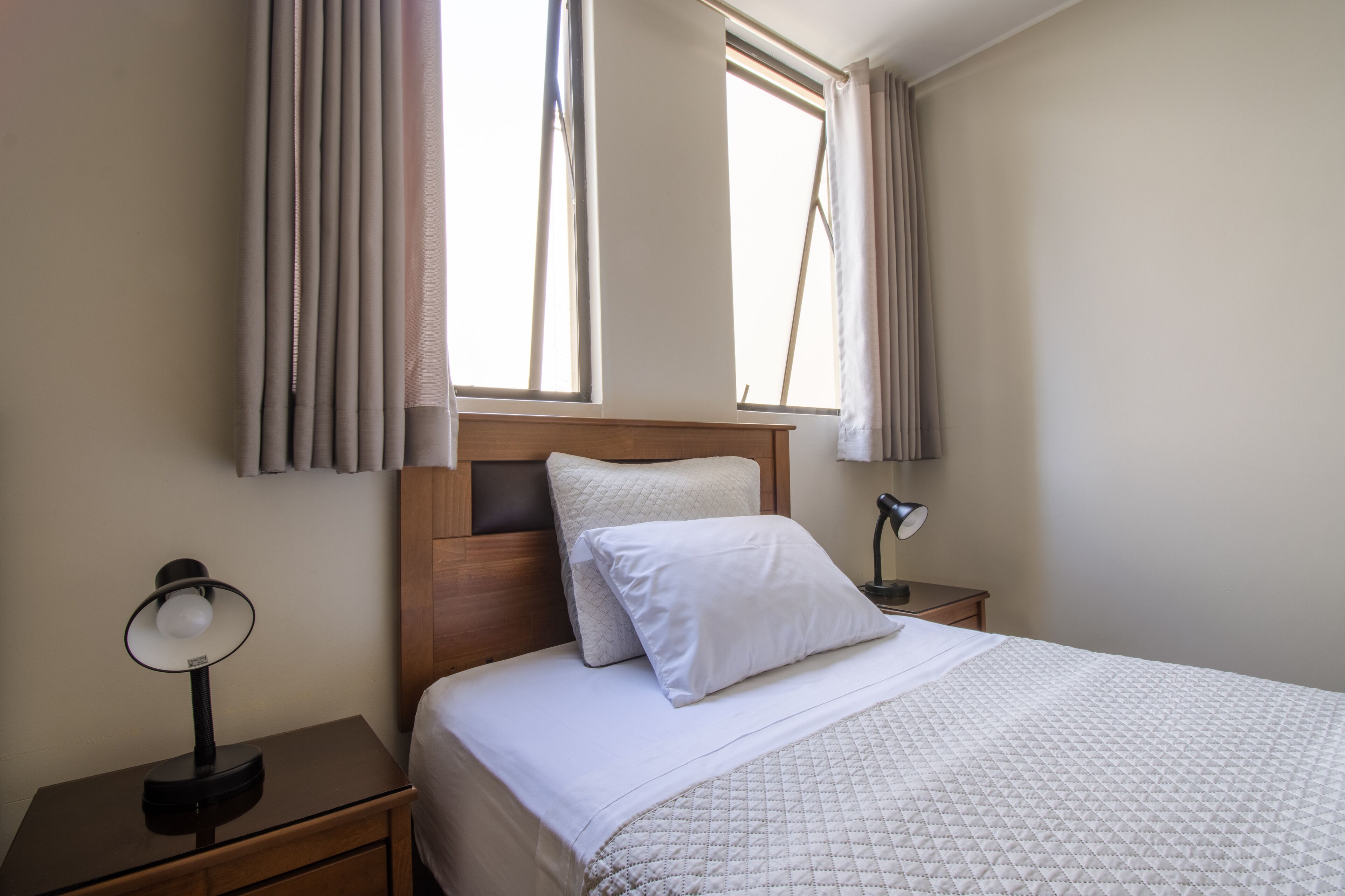 A neatly made bed with a quilted cover, a bedside lamp, and a nightstand with a lamp.