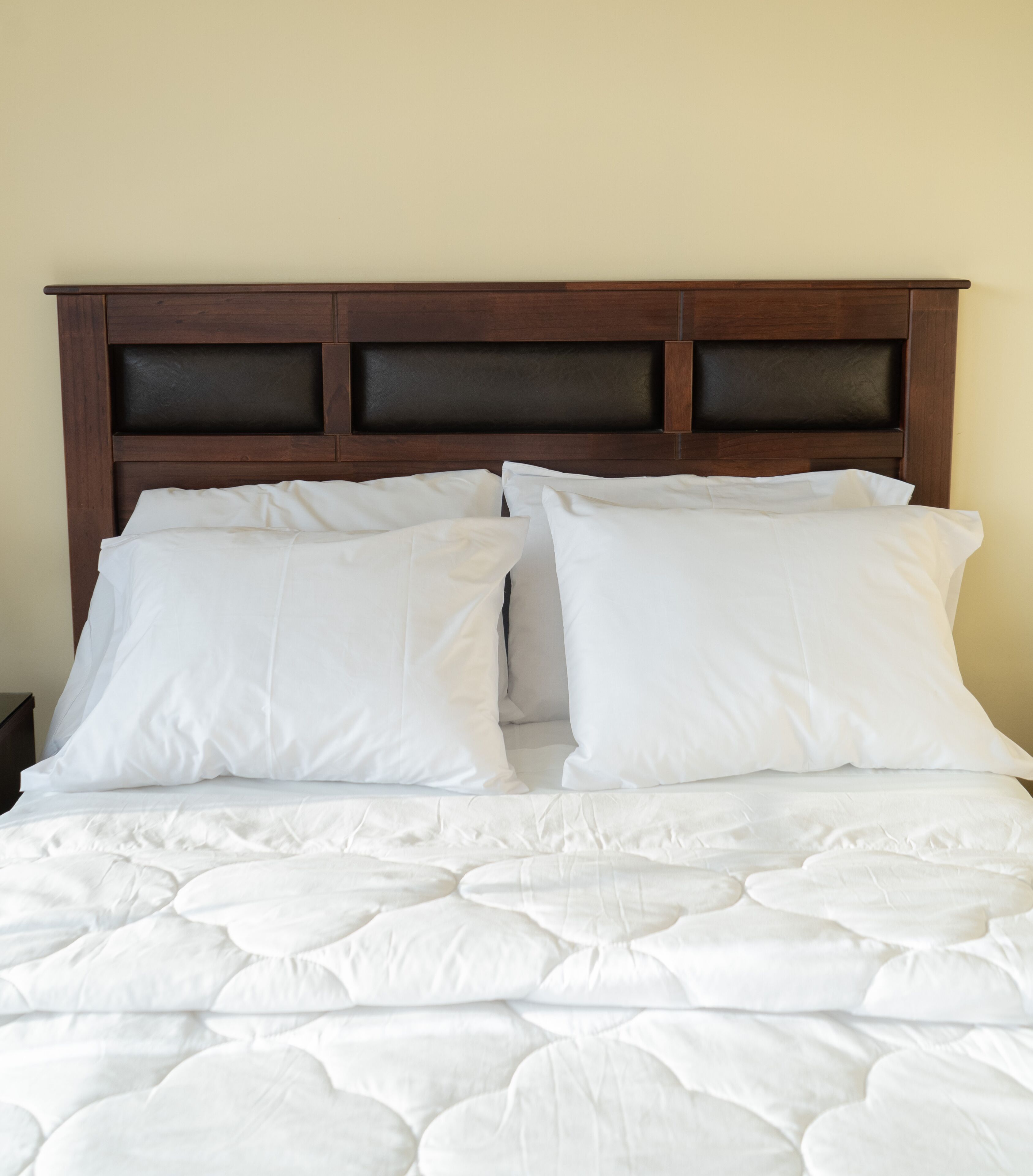 A neatly made bed with white bedding and a wooden headboard.