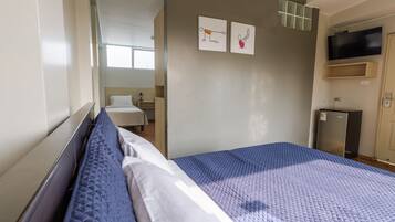 Una habitación de hotel con una cama, un televisor montado en la pared y un refrigerador pequeño.