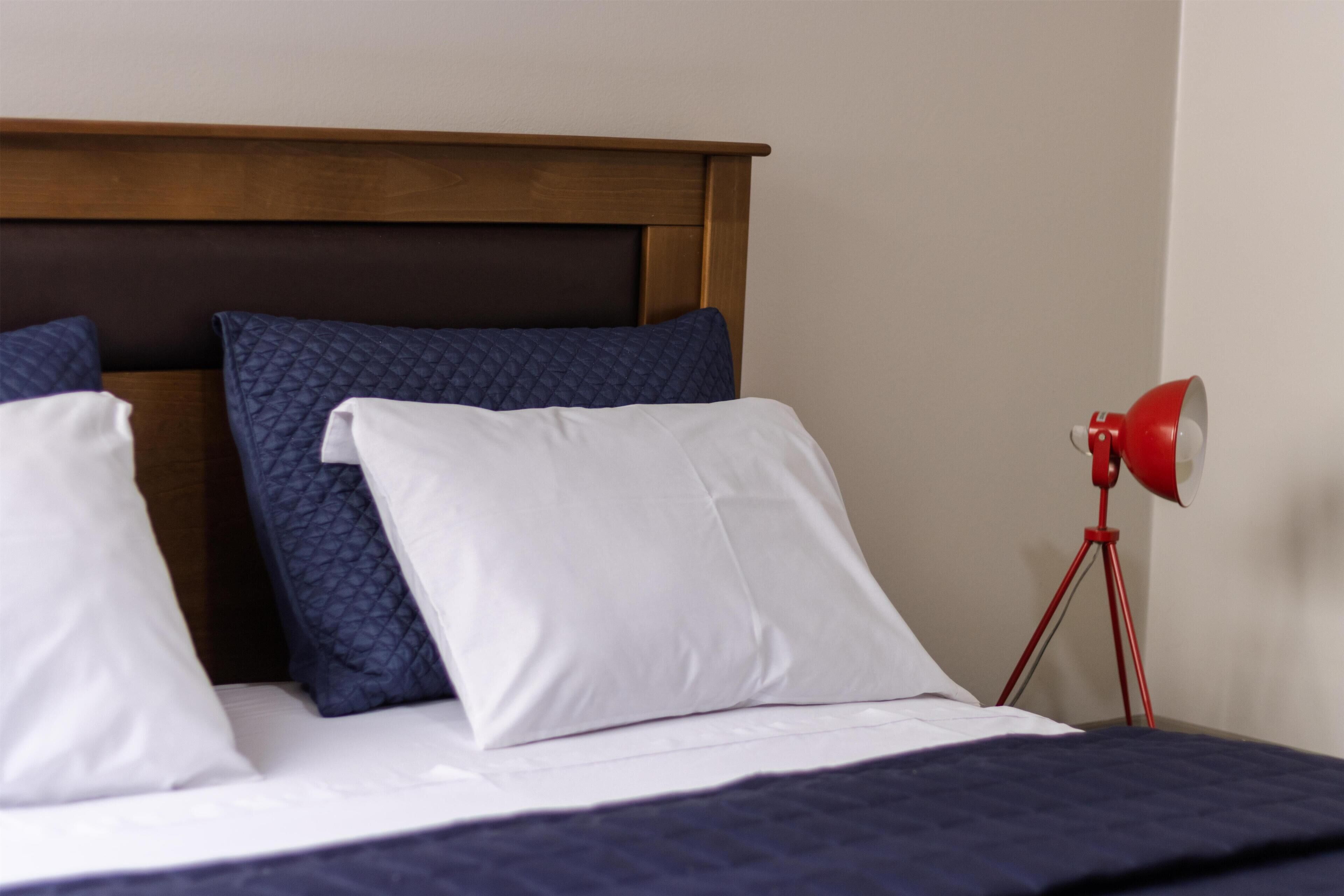 A bed with a wooden headboard, white and blue pillows, and a red floor lamp.