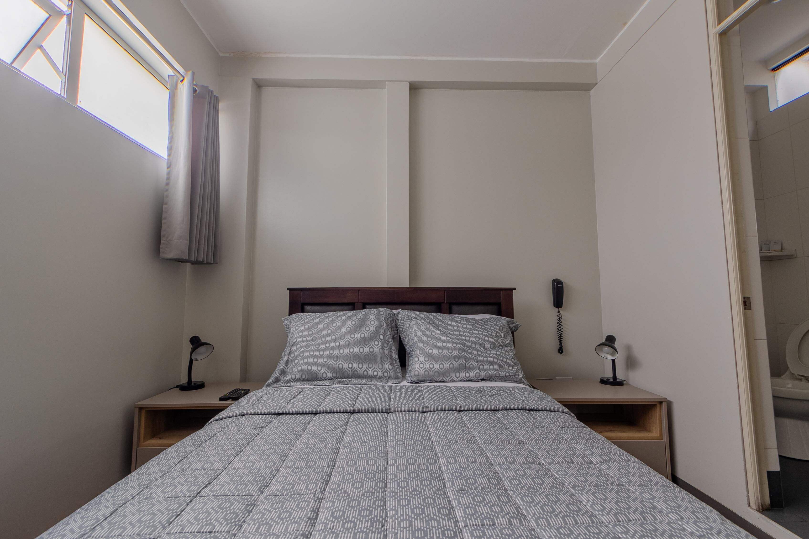 Un dormitorio con una cama, dos mesitas de noche, un teléfono y una ventana con cortinas.