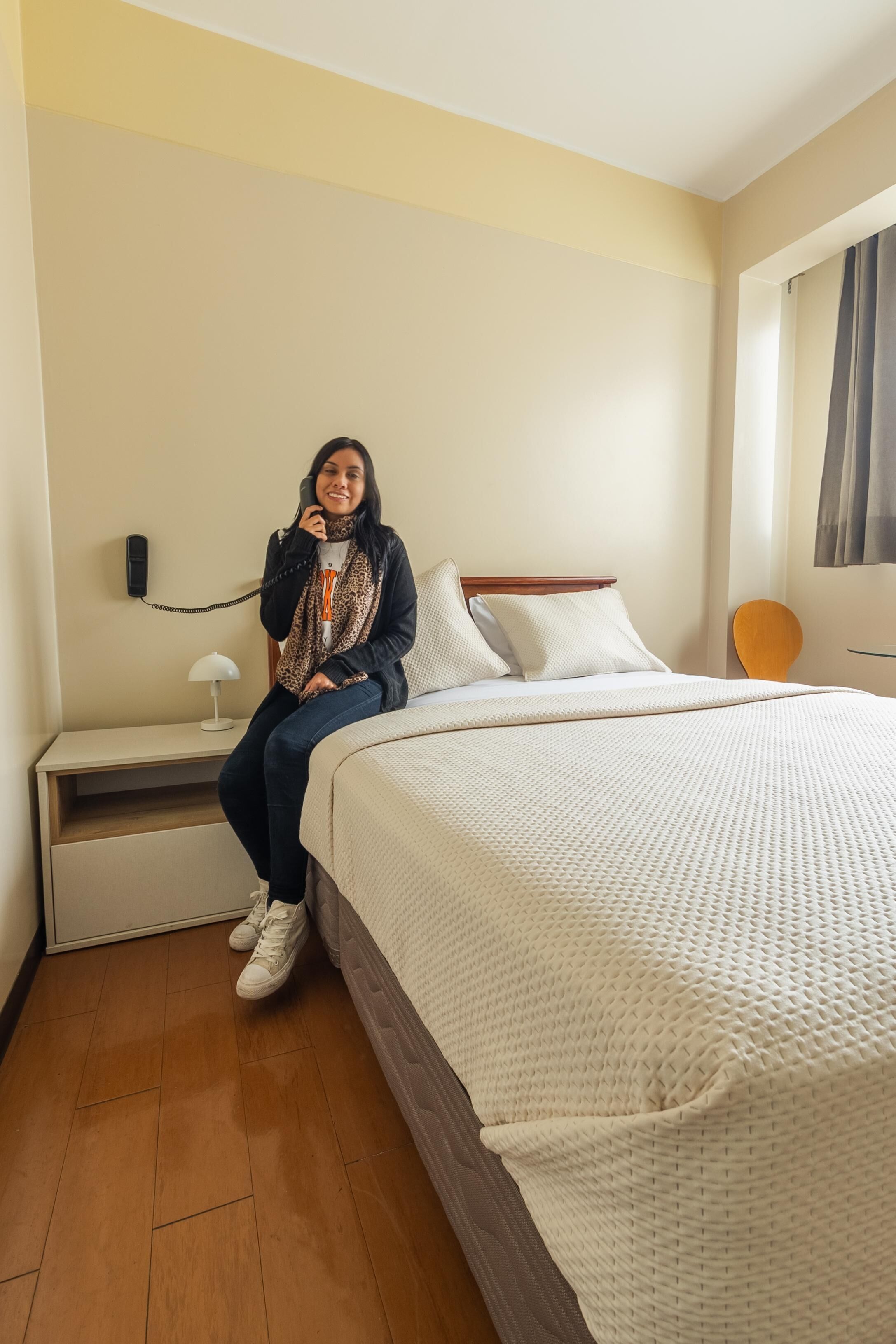 Una habitación de hotel con cama, mesita de noche, lámpara y teléfono.