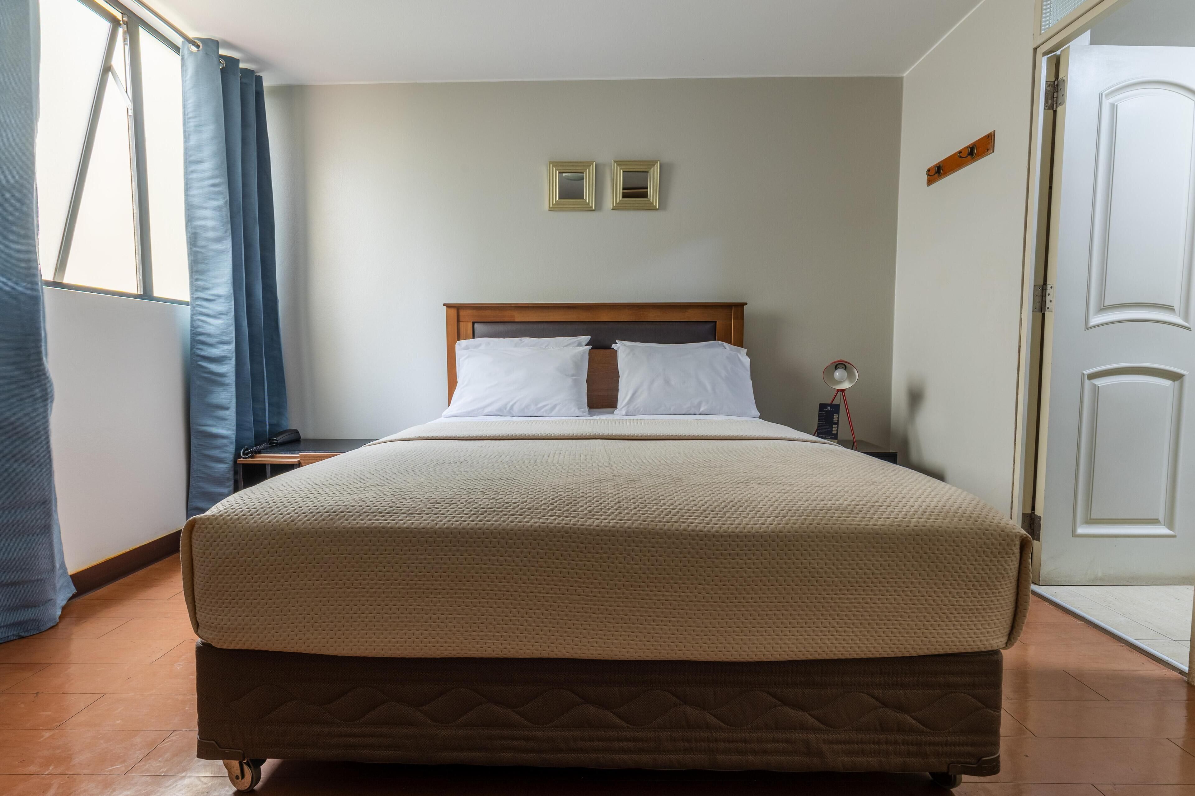 Una habitación de hotel con una cama, una mesita de noche, una lámpara y una puerta.
