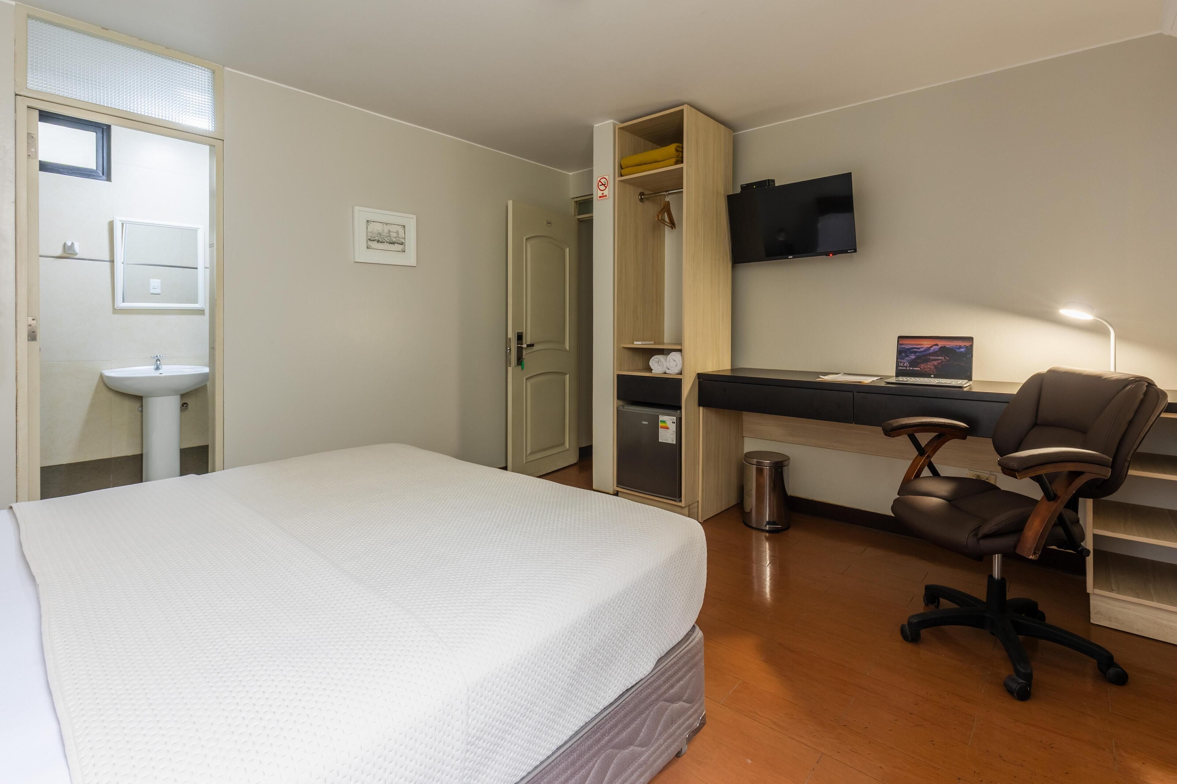 Una habitación de hotel con cama, escritorio con computadora, silla, televisor y armario.