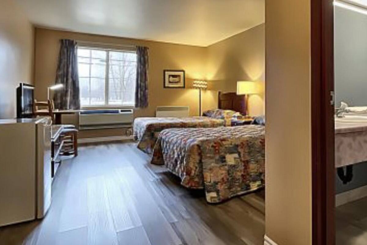 Habitación de hotel con dos camas, una ventana con cortinas, una mesita de noche y un baño con inodoro y lavabo.