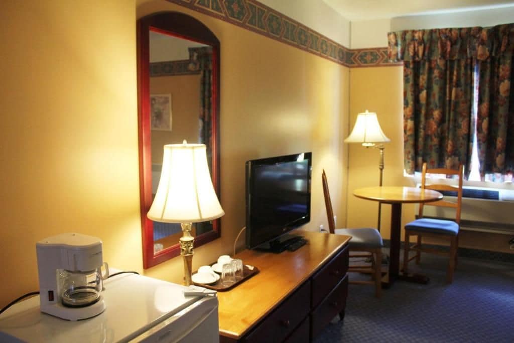 A hotel room with a television, coffee maker, and a dining area with a table and chairs.