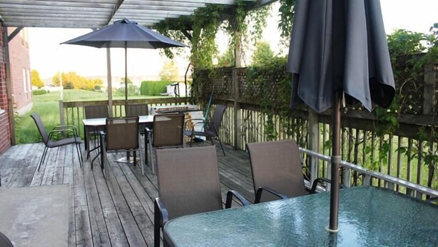An outdoor patio with a wooden deck, metal chairs, a glass table, and a black umbrella. - Hôtel Le Portneuvois (Portneuf)
