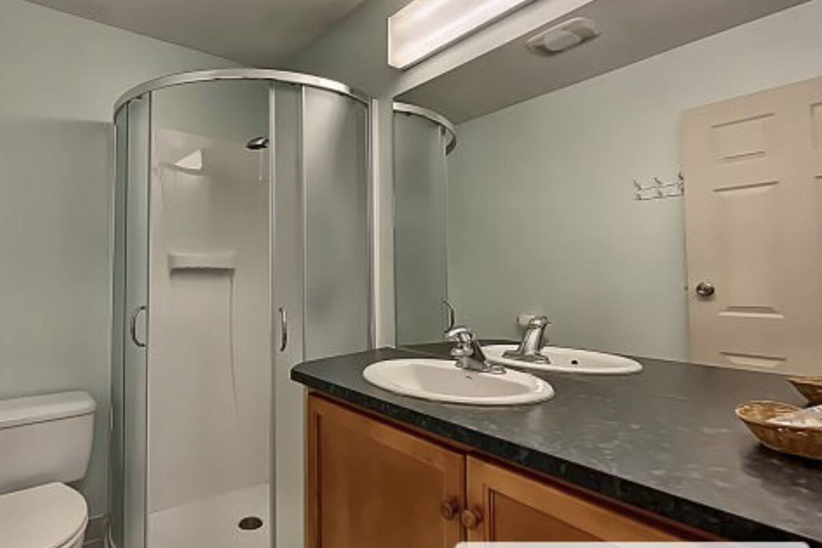 Un baño con inodoro, cabina de ducha de vidrio y dos lavamanos.