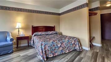 Habitación de hotel con cama, mesita de noche, lámpara, sofá azul y suelo de madera.